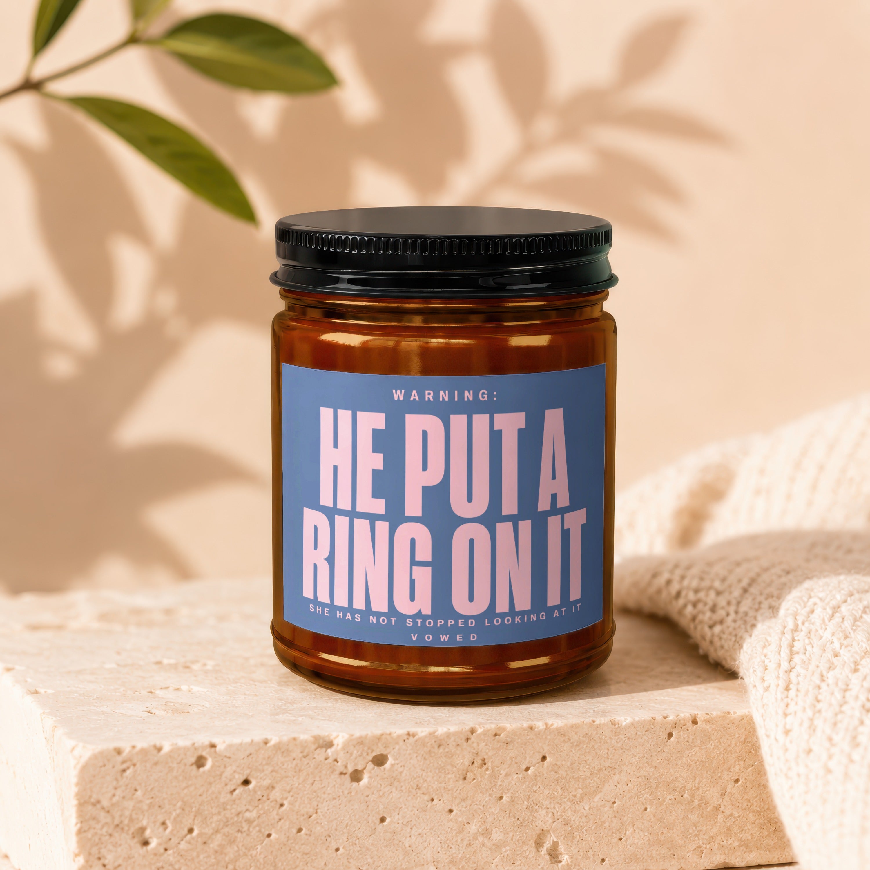Candle with blue label reading "WARNING: HE PUT A RING ON IT (SHE HAS NOT STOPPED LOOKING AT IT) VOWED."