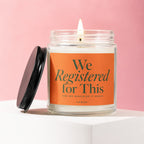 Lit candle in a glass jar with an orange label that reads "We Registered for This".