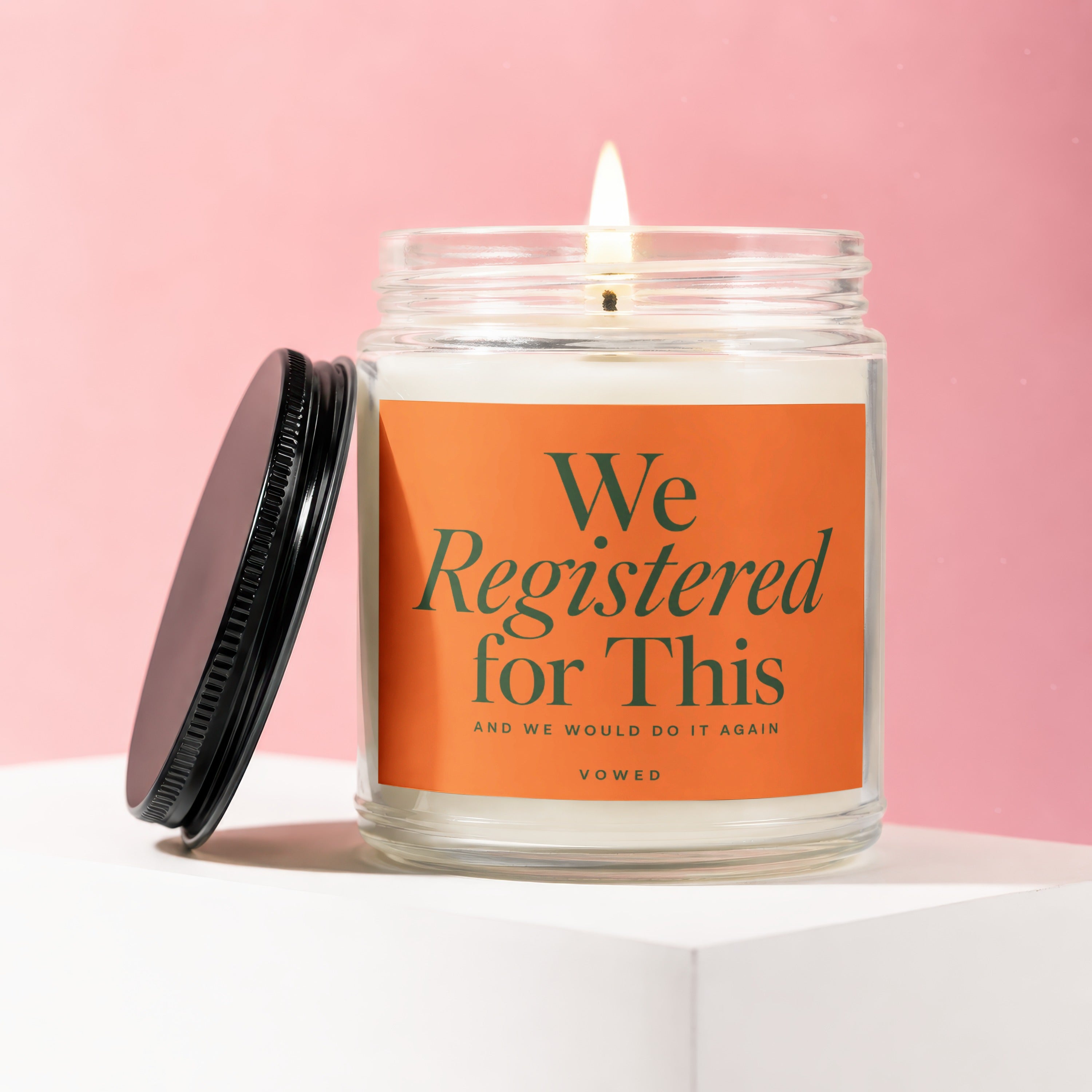 Lit candle in a glass jar with an orange label that reads "We Registered for This".