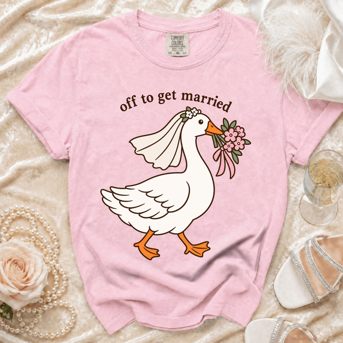 Pink t-shirt with a graphic of a goose wearing a veil and holding flowers, reading "off to get married".