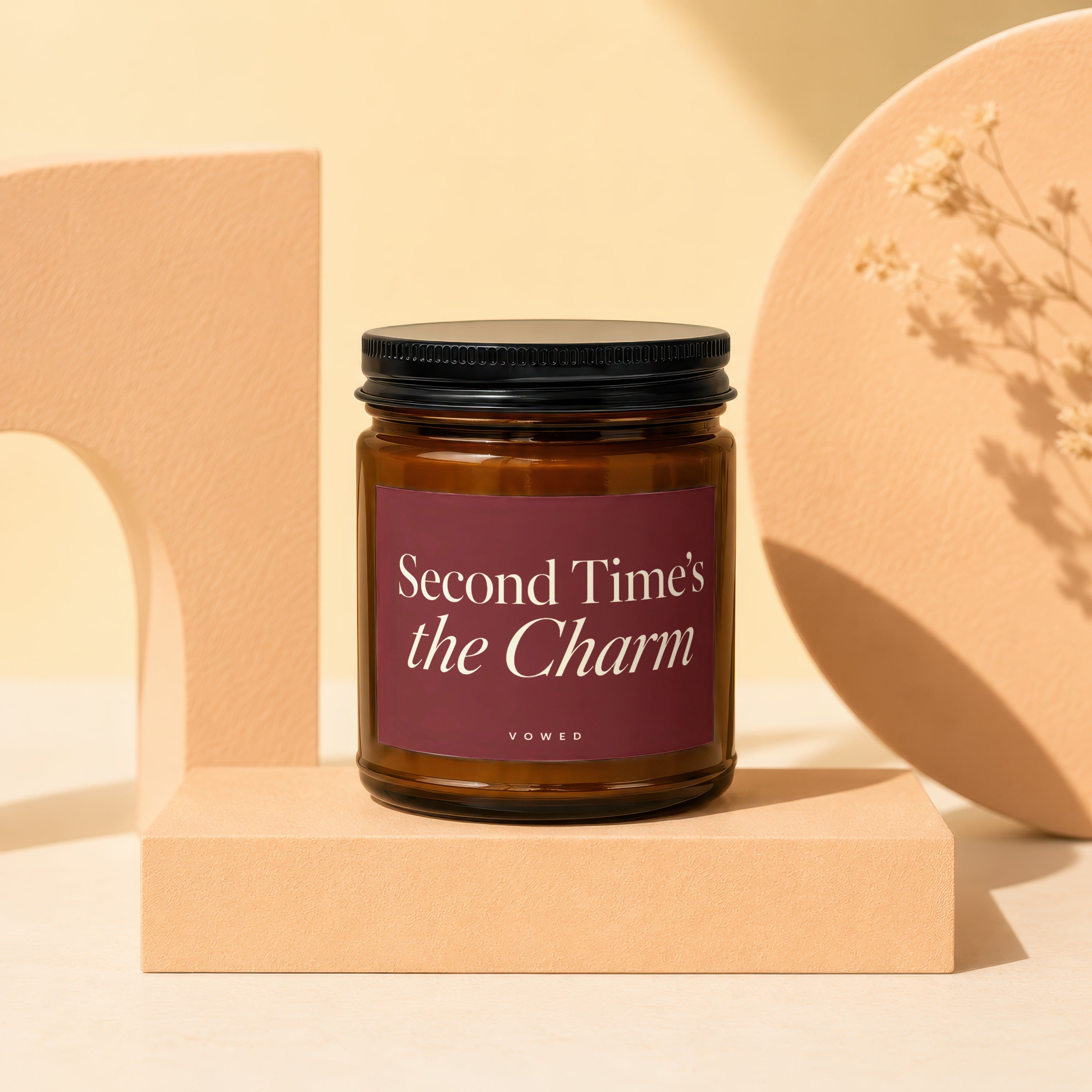 Amber glass candle with black lid, label reads "Second Time's the Charm"