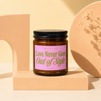 Brown glass candle with pink label reading "Love Never Goes Out of Style".