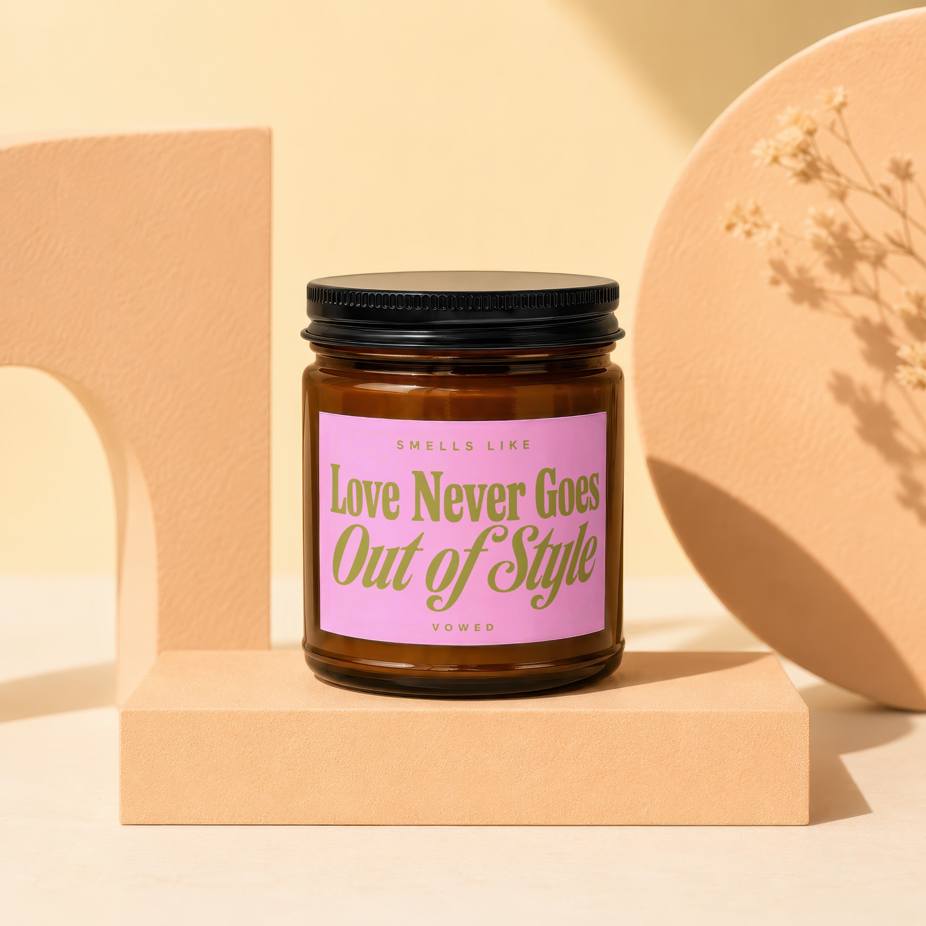 Brown glass candle with pink label reading "Love Never Goes Out of Style".
