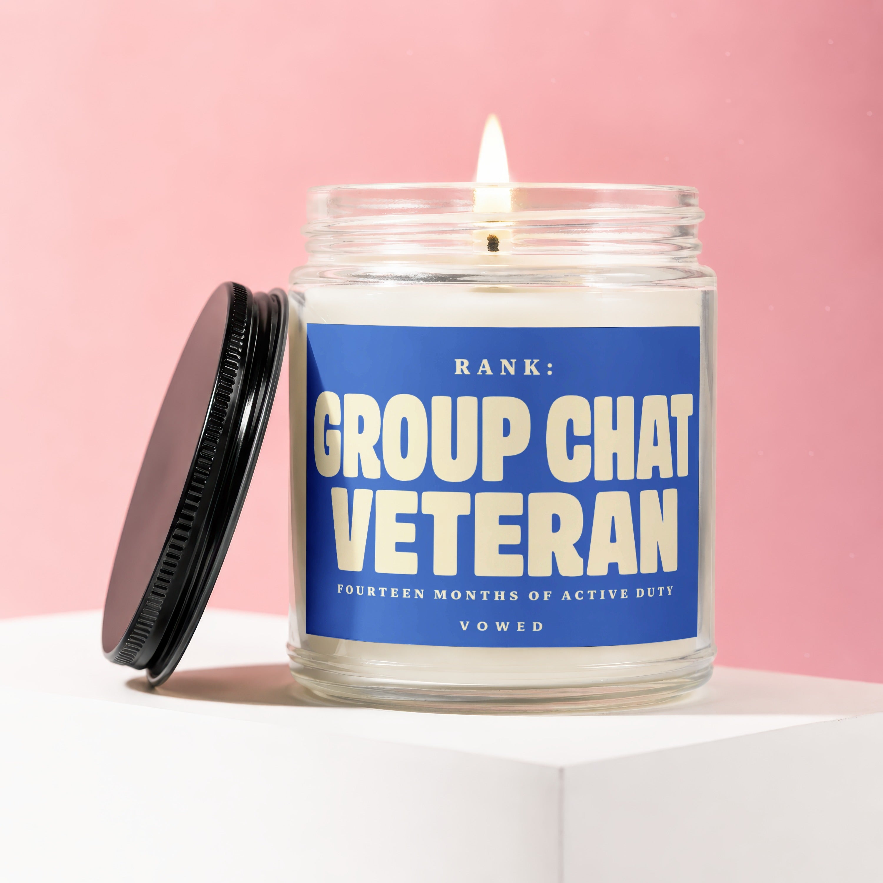 Jar candle with lit wick and black lid. Label reads "RANK: GROUP CHAT VETERAN".