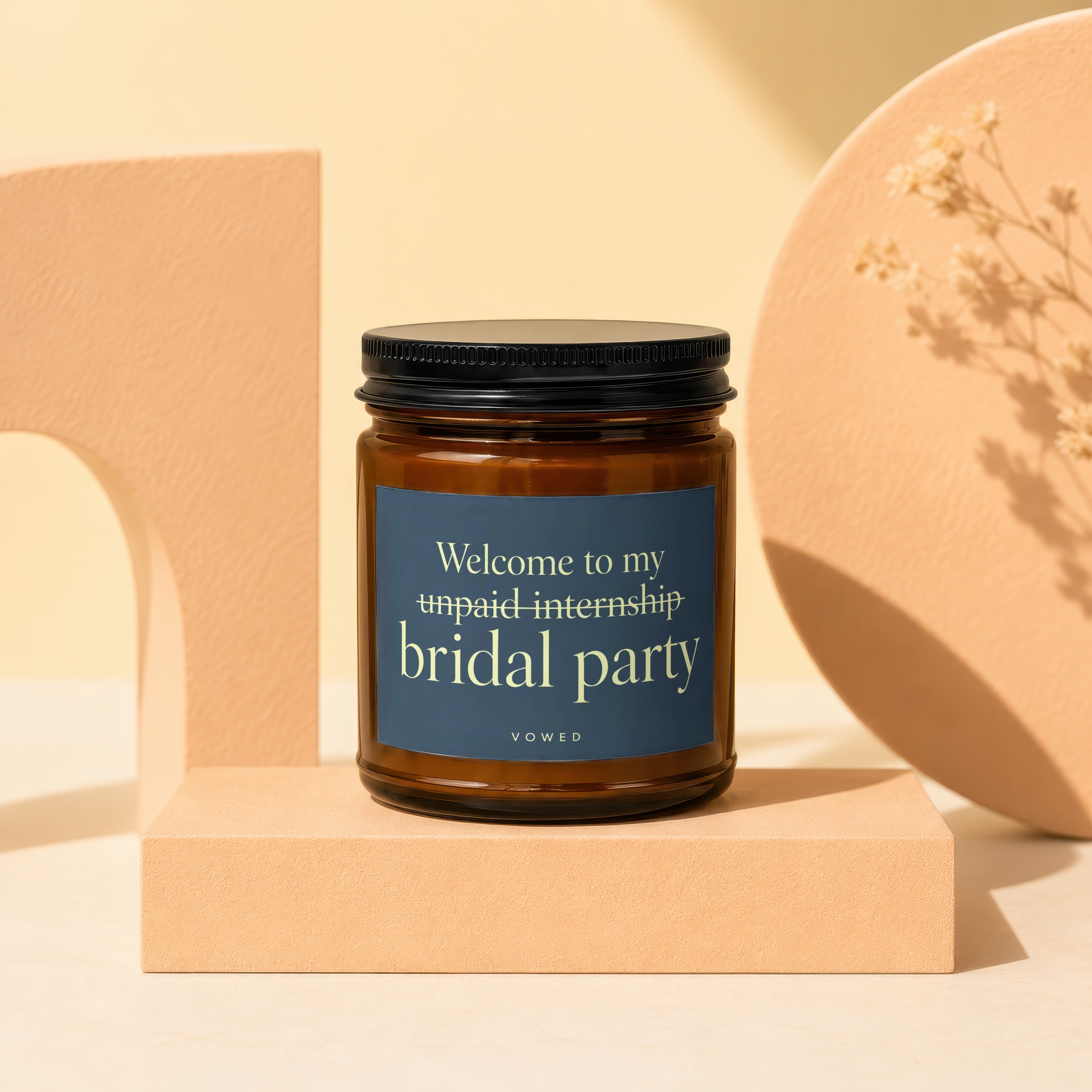 Amber glass candle with dark blue label reading "Welcome to my unpaid internship bridal party Vowed."
