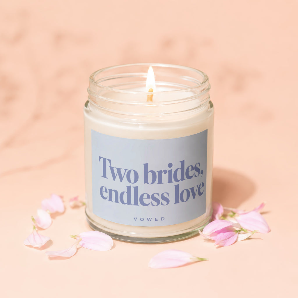 Candle with text "Two brides, endless love" surrounded by pink petals.