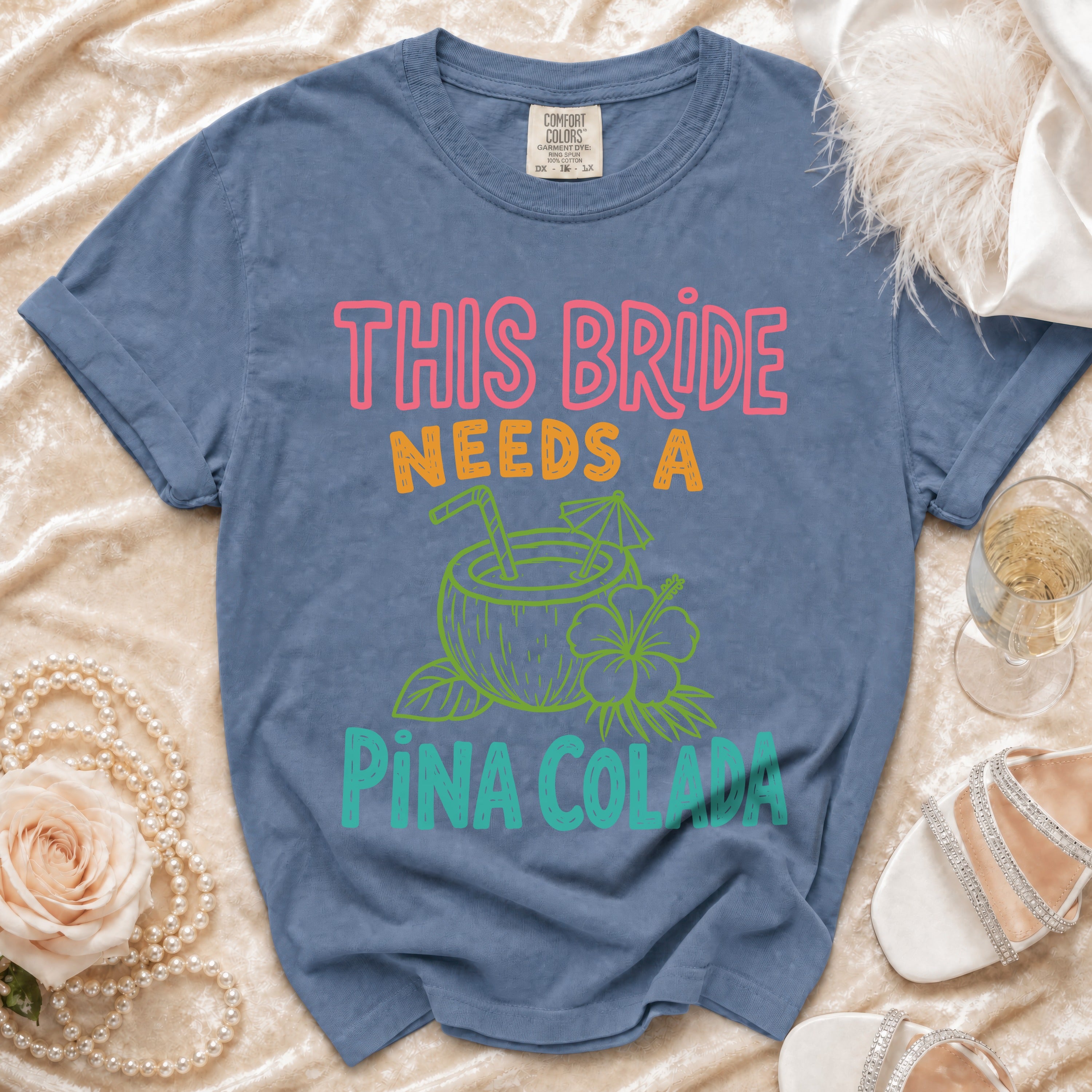 Blue t-shirt with "This Bride Needs A Piña Colada" graphic and tropical drink.