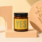 Brown glass candle with yellow label saying "SMELLS LIKE YES THE ANSWER WAS ALWAYS YES".