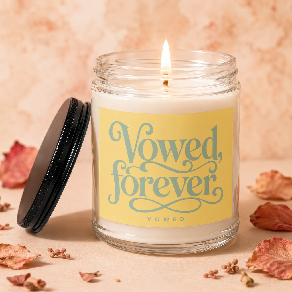 Glass jar candle with lit wick and a yellow label that reads "Vowed, forever"