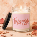 "To-be-weds" candle with pink label, lit flame, and decorative leaves.