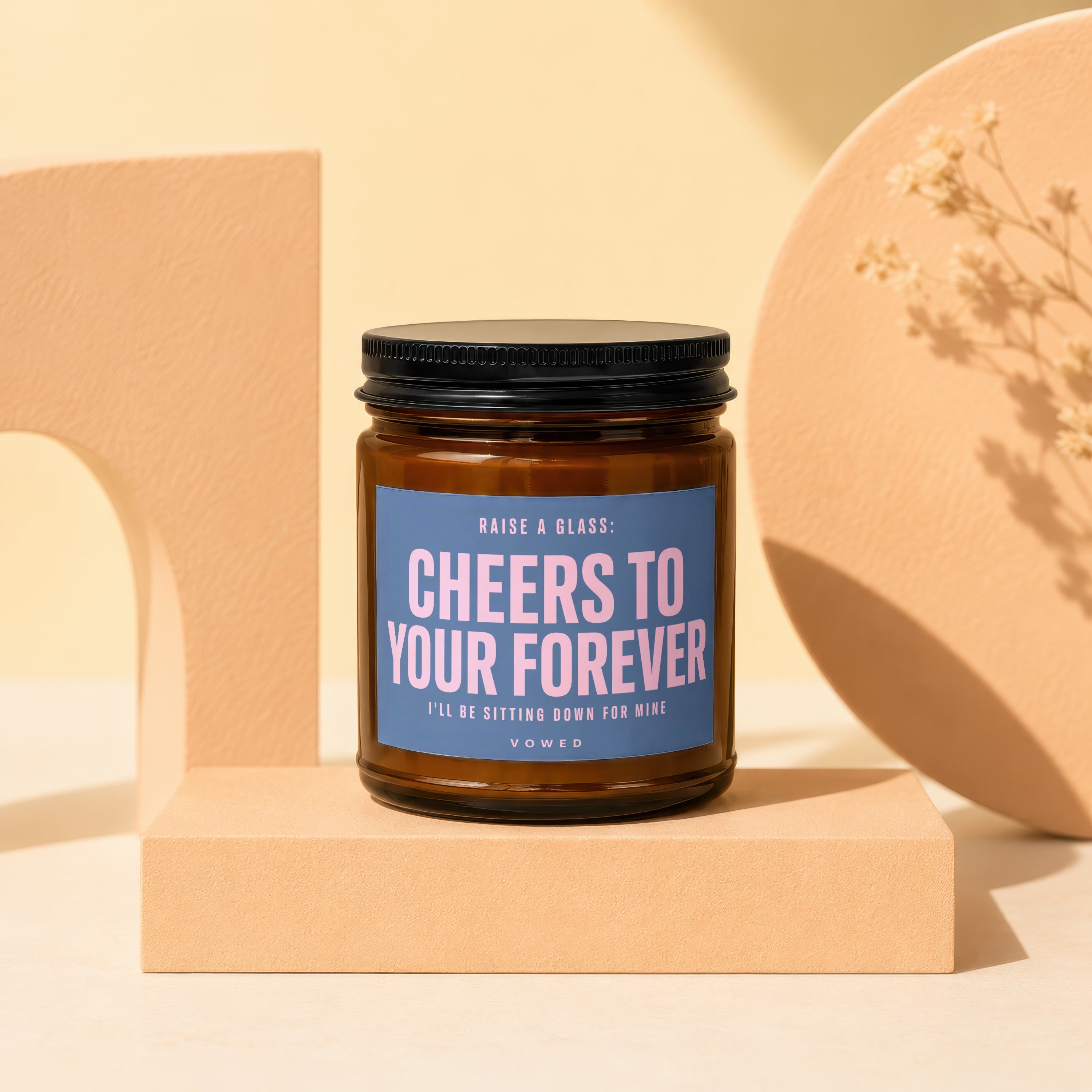 Amber glass candle with black lid, blue label reads "Cheers to your forever".