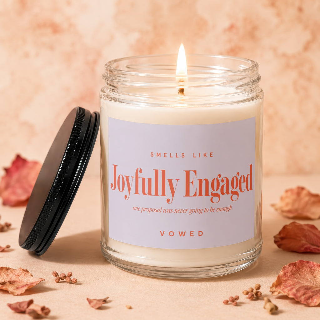 Glass candle with "Joyfully Engaged" on label, lid off, and flame lit.