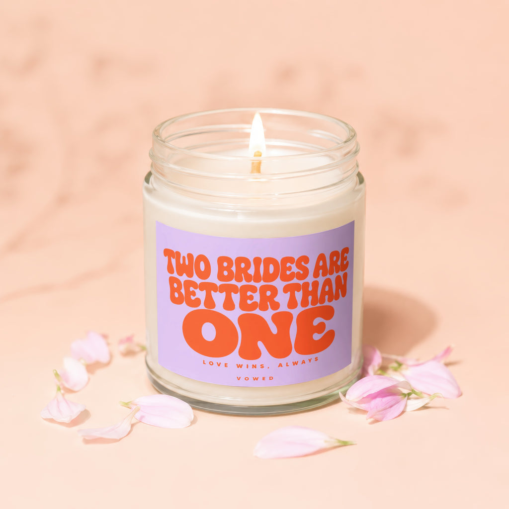 Candle with "Two Brides Are Better Than One" text and pink flower petals.
