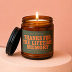 Amber candle with lid off, burning flame, reads "Thanks for the lifetime memory".
