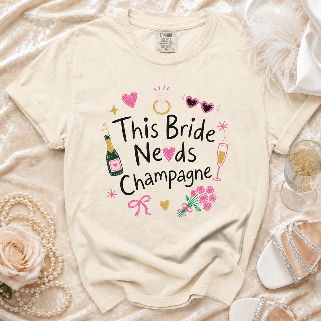 Cream t-shirt with "This Bride Needs Champagne" graphic and bridal accessories.