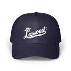 A dark blue baseball cap with white embroidered text reading Lassoed centered on the front panels.