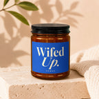 Amber candle in a glass jar with a blue label that reads "Wifed Up. vowed".