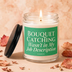 A lit candle in a glass jar with a green label reading "BOUQUET CATCHING Wasn't in My Job Description".