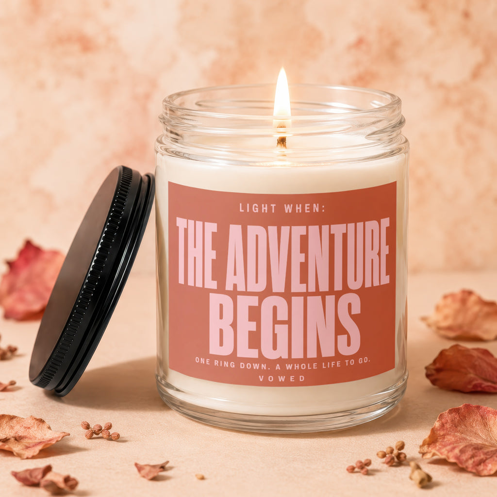 Candle with "The Adventure Begins" text for weddings, surrounded by dried leaves and petals.