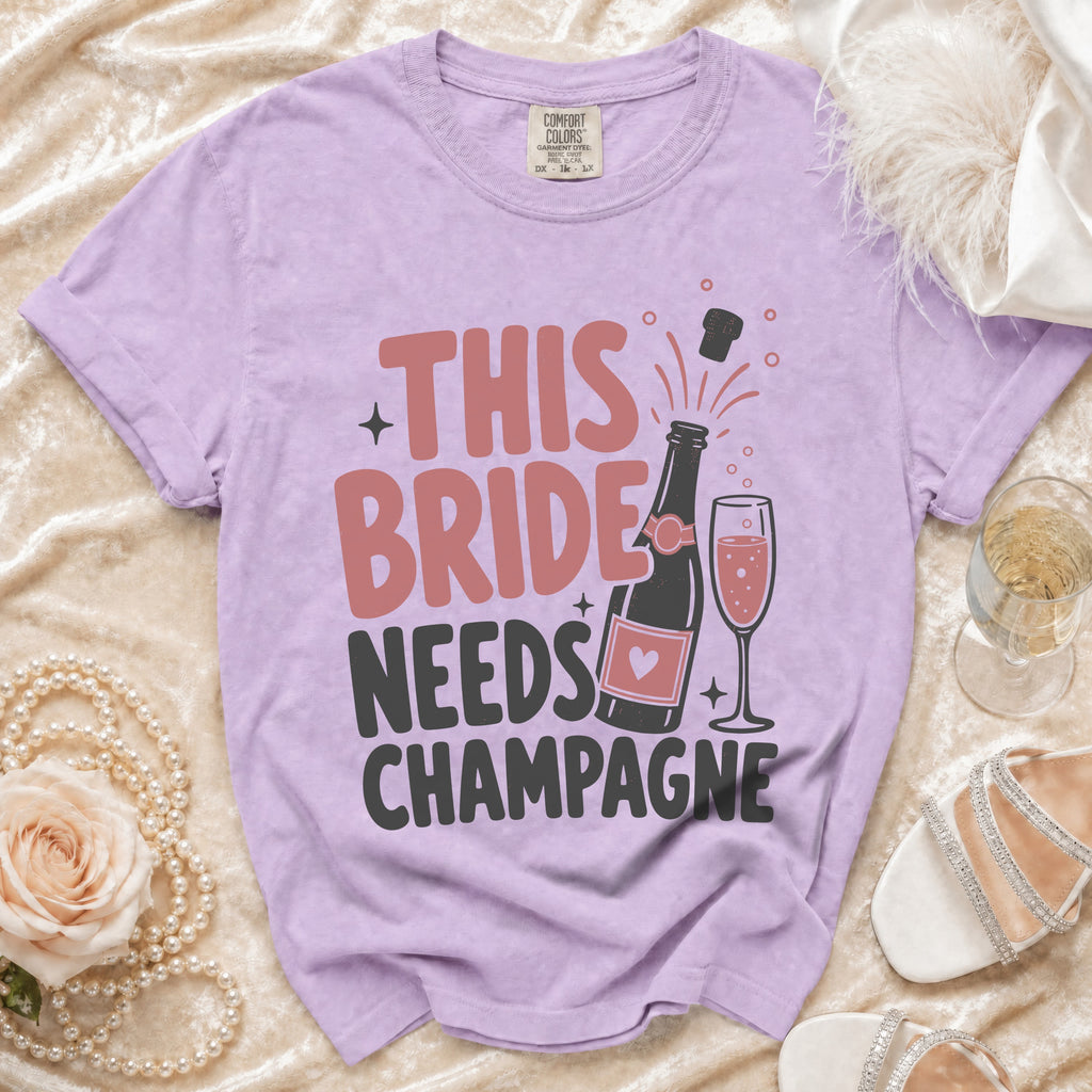 Purple t-shirt with "THIS BRIDE NEEDS CHAMPAGNE" text and champagne bottle graphic.