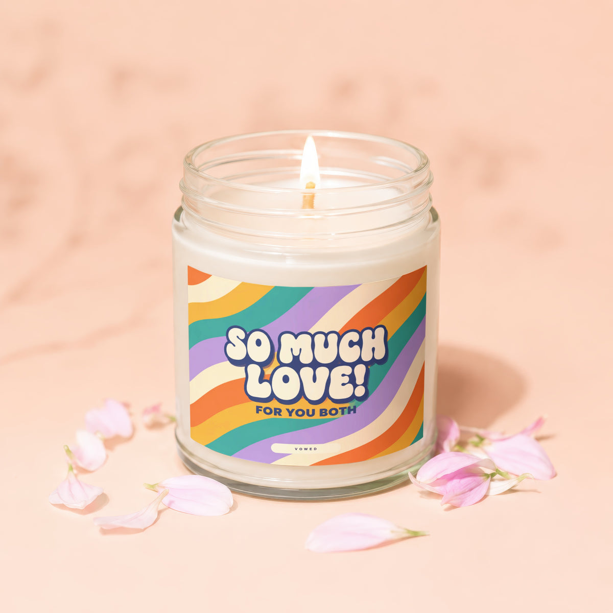 Lit candle in a jar with a "So Much Love! For You Both" label and petals.