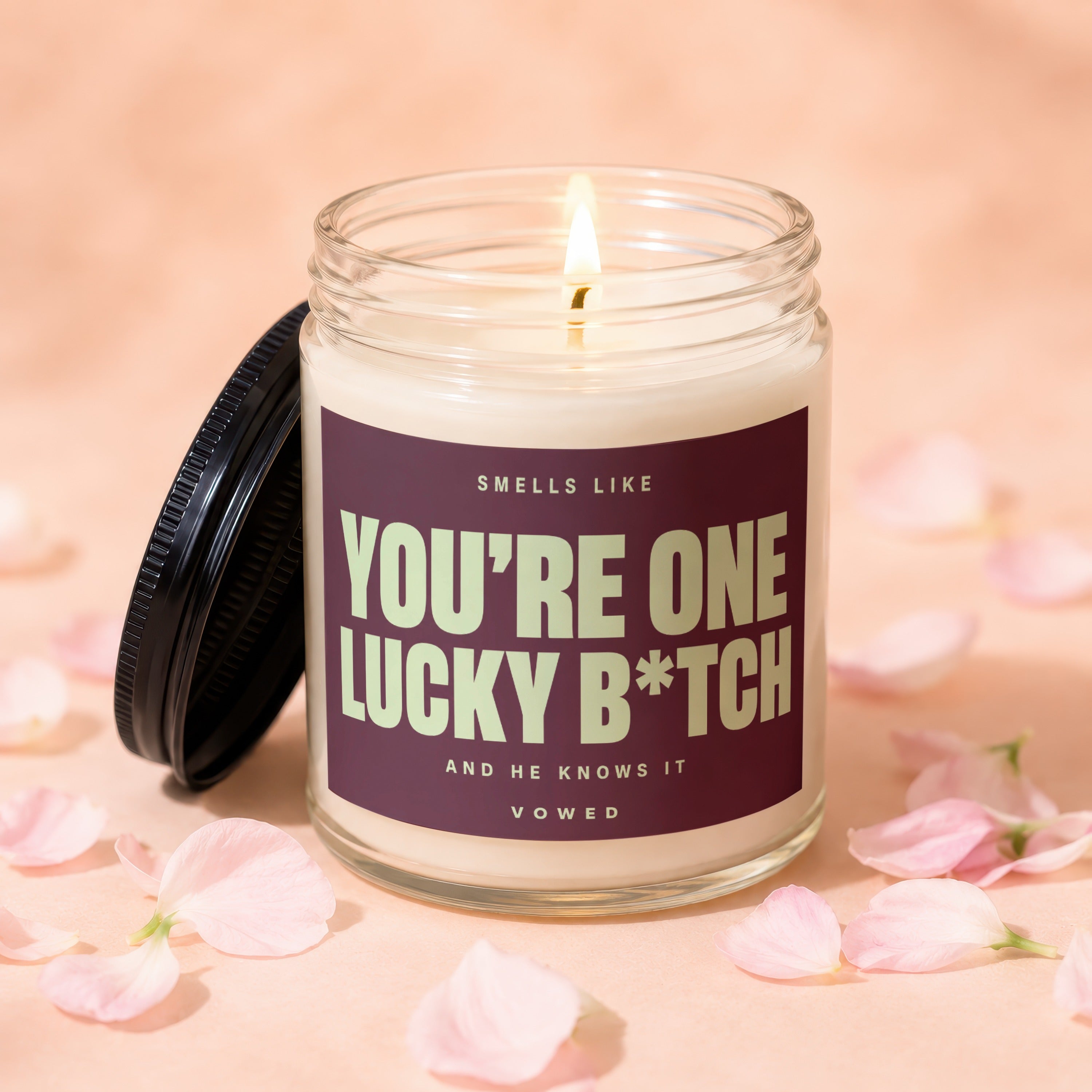 Glass jar candle lit with text "You're One Lucky B*tch" and "Vowed".