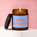 Brown glass candle with lit wick and black lid, "entering bridesmaid era." text.