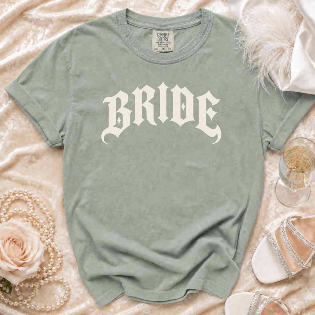 Grey t-shirt with "BRIDE" text, draped on velvet with pearls and champagne.