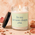 Glass candle with lit wick, featuring text "In my last-name-changing era. VOWED".