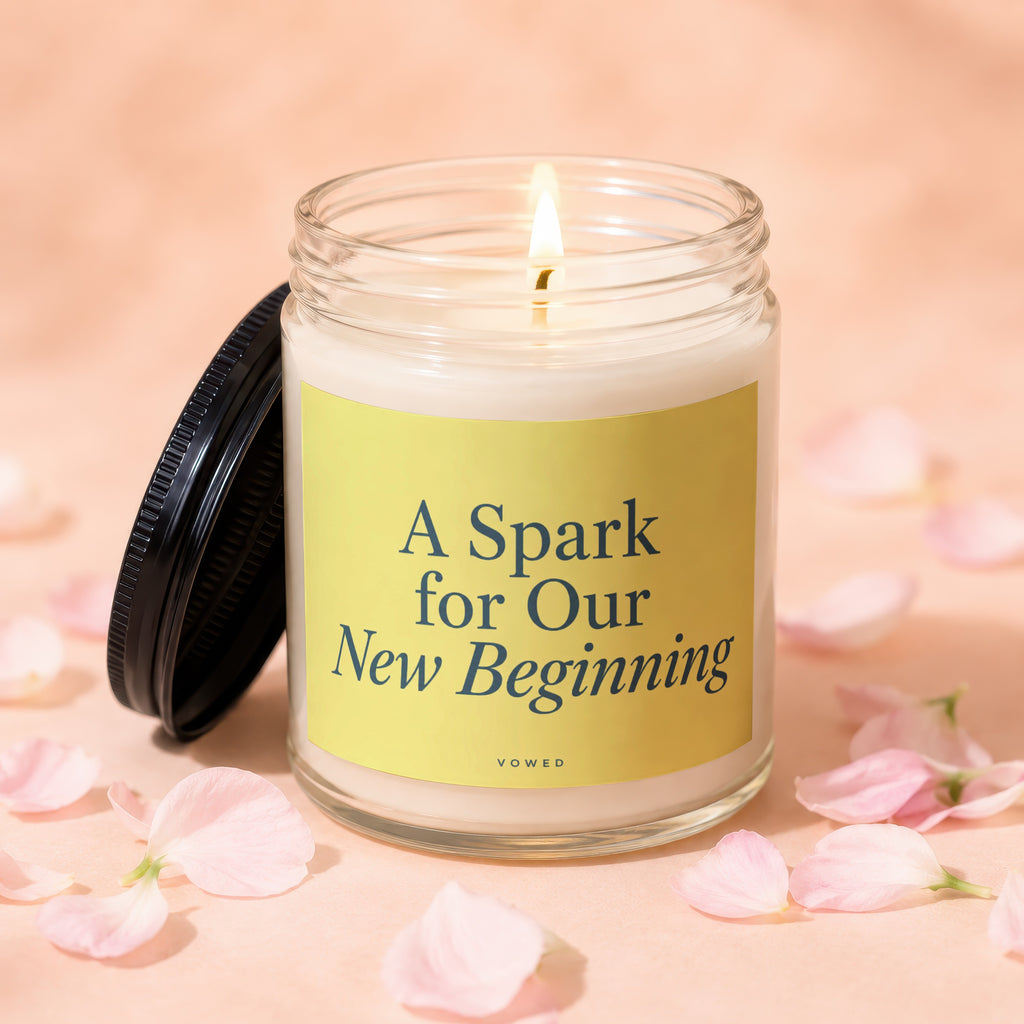 Glass jar candle with a lit wick and a yellow label that reads "A Spark for Our New Beginning".