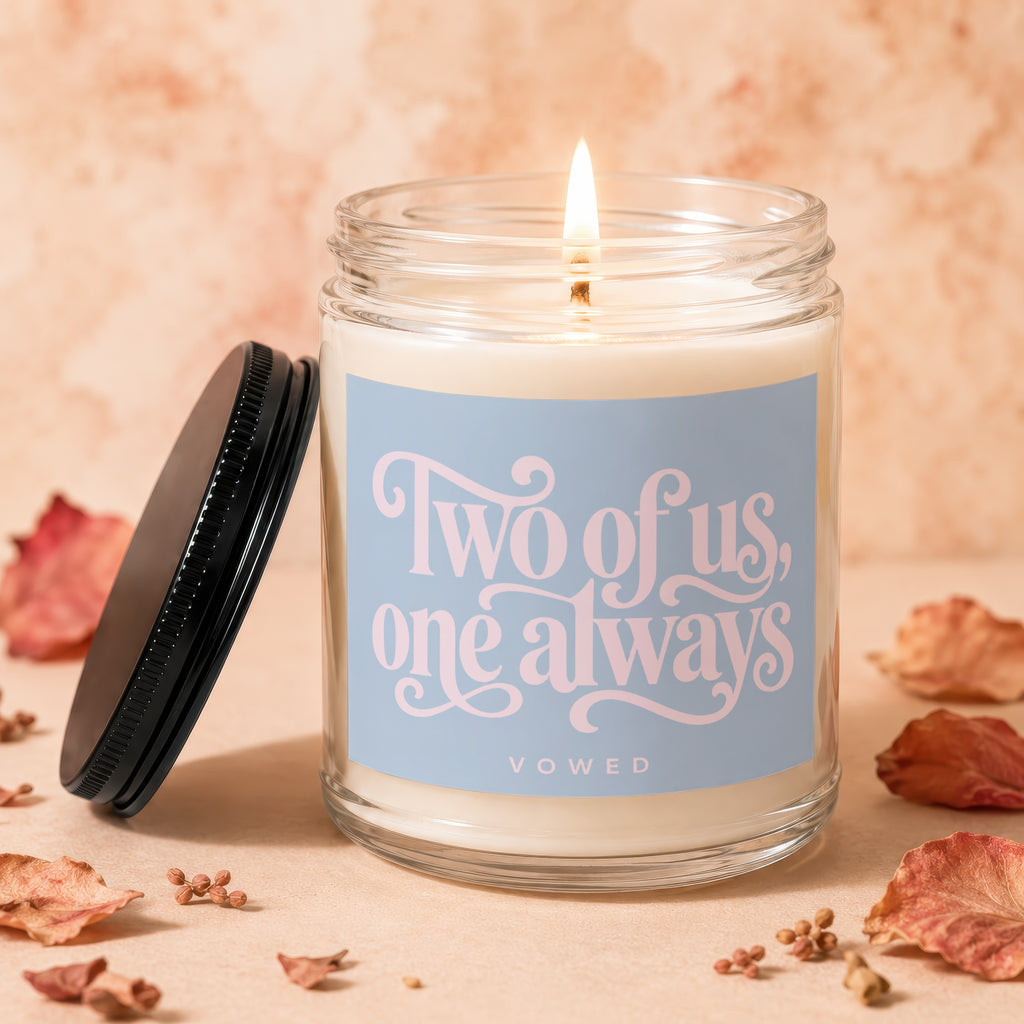 Glass candle with lit wick and "Two of us, one always" text.