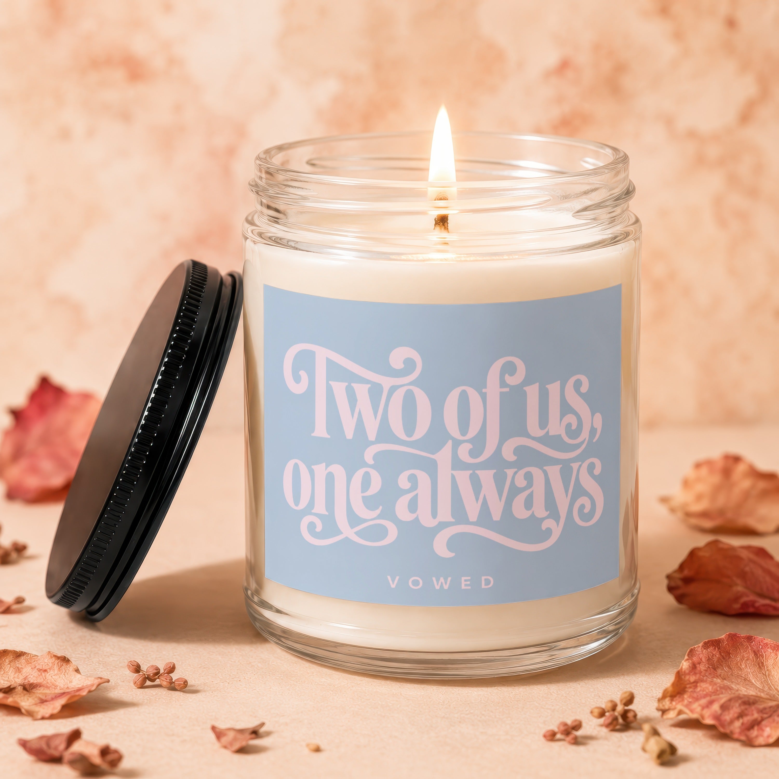 Glass candle with lit wick and "Two of us, one always" text.