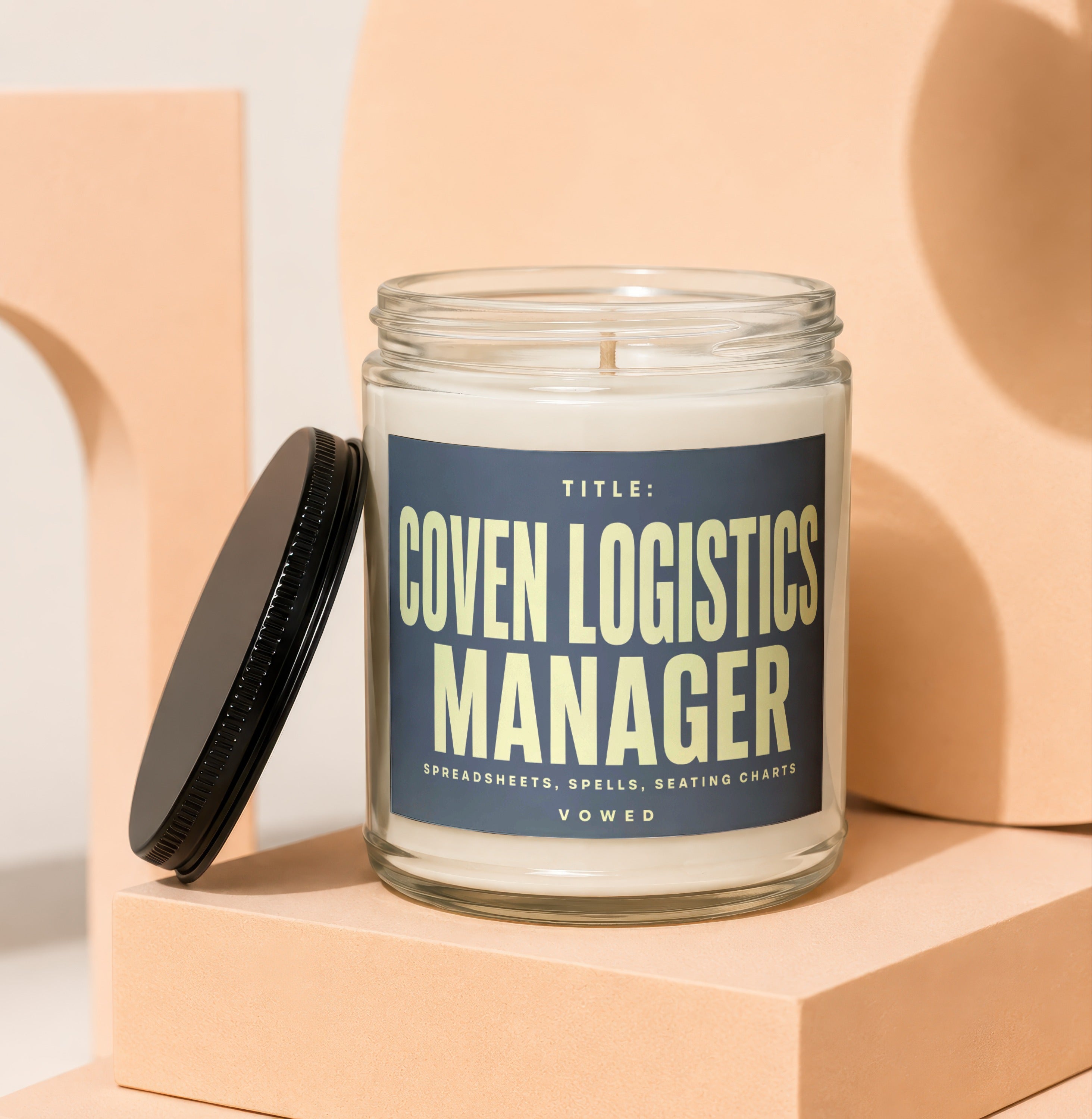 Glass candle with navy label reading "Coven Logistics Manager" and "Vowed".