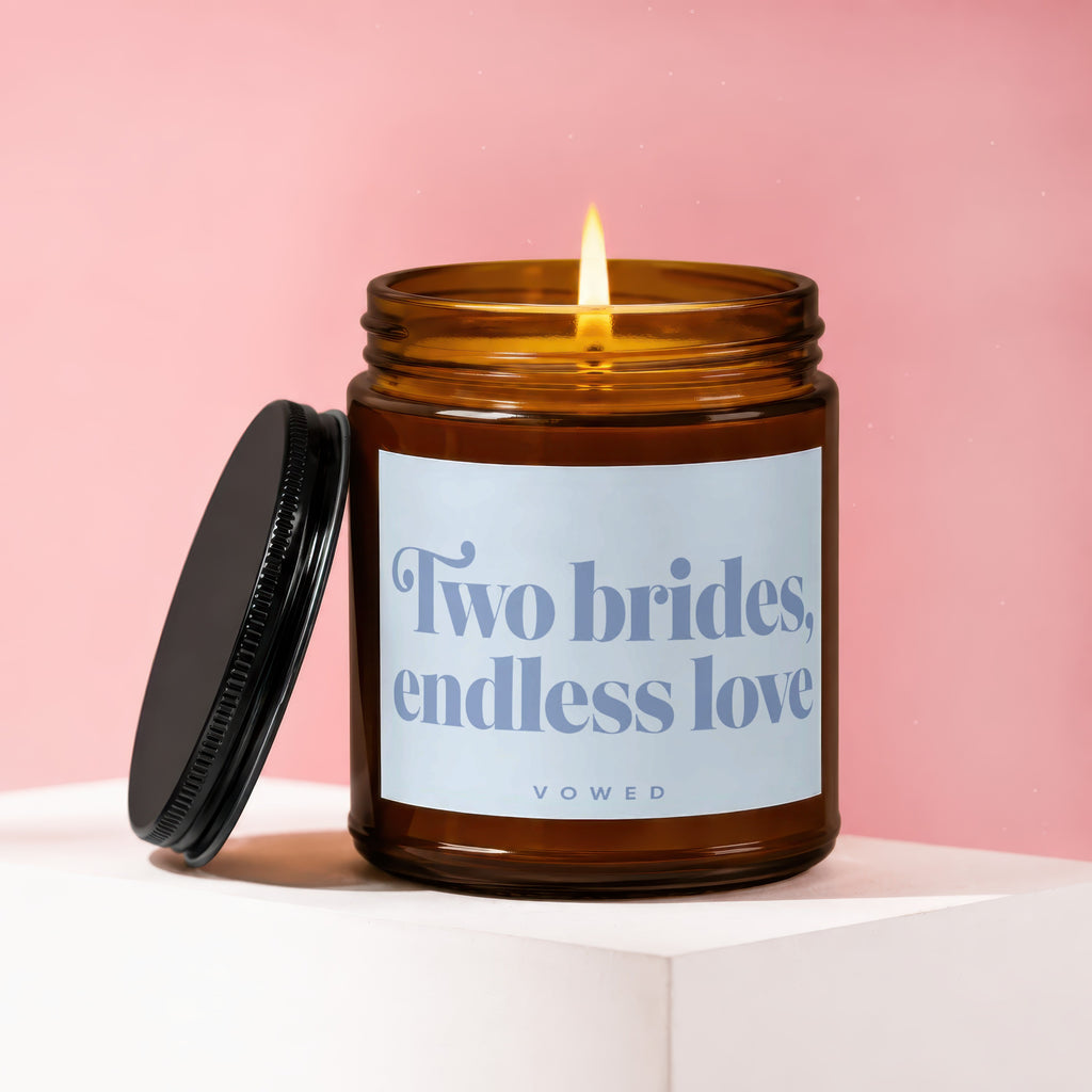 Amber jar candle with lit flame, lid askew, reads "Two brides, endless love"
