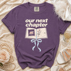 Purple t-shirt with "our next chapter" text and an open book graphic.