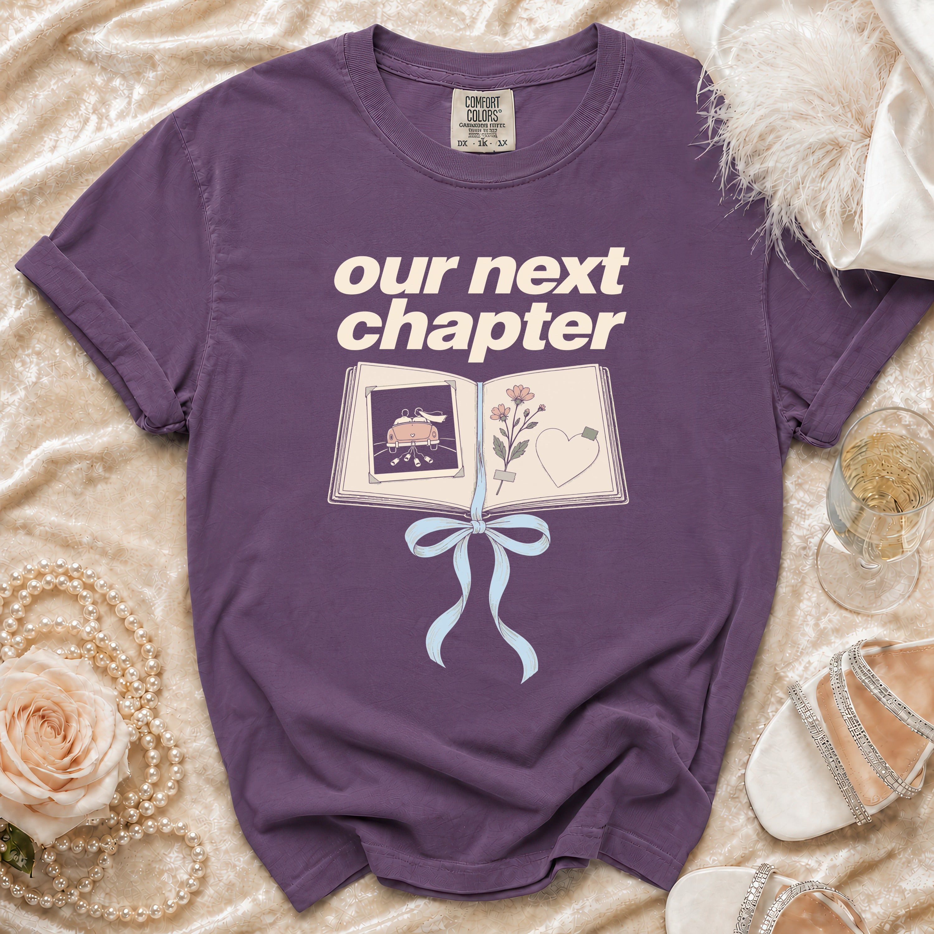 Purple t-shirt with "our next chapter" text and an open book graphic.