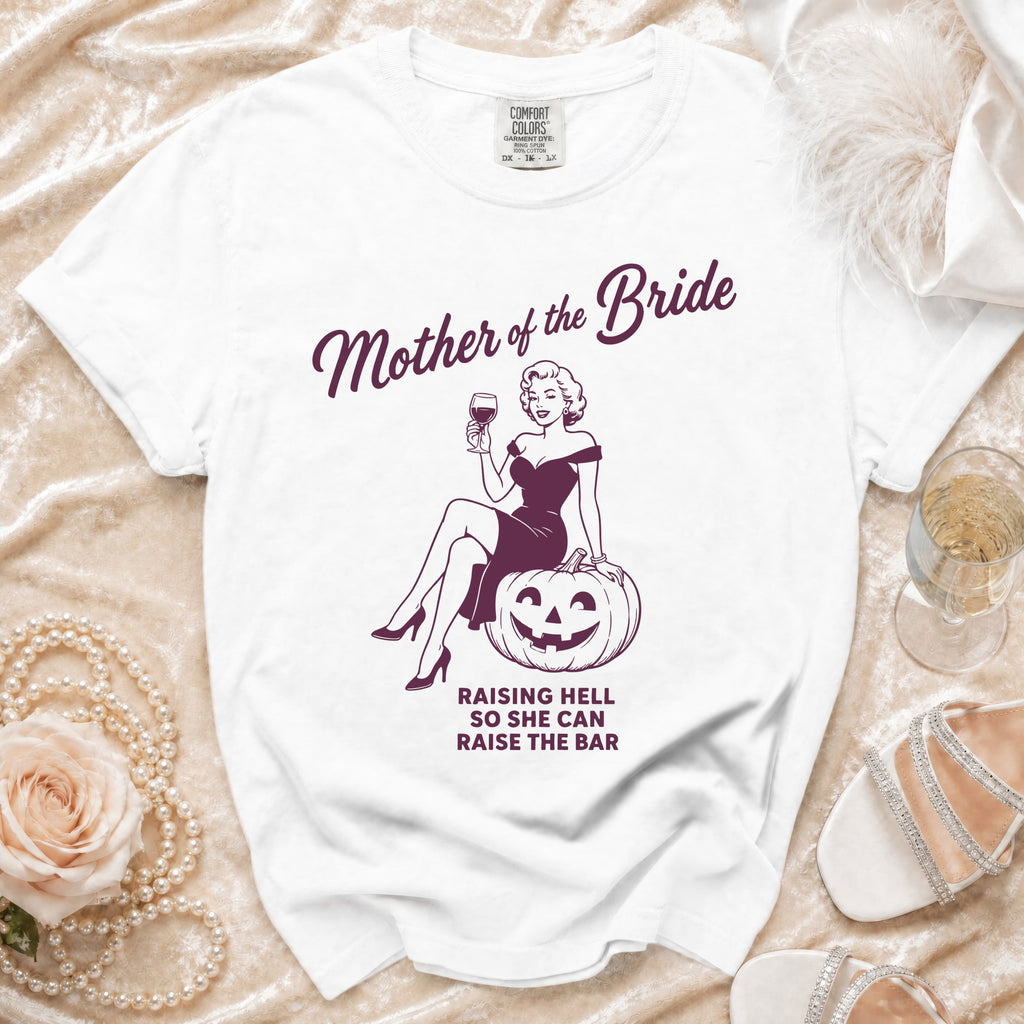 White t-shirt with "Mother of the Bride" design and text "Raising Hell So She Can Raise The Bar".