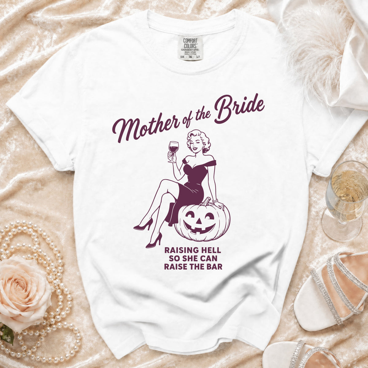 White t-shirt with "Mother of the Bride" design and text "Raising Hell So She Can Raise The Bar".