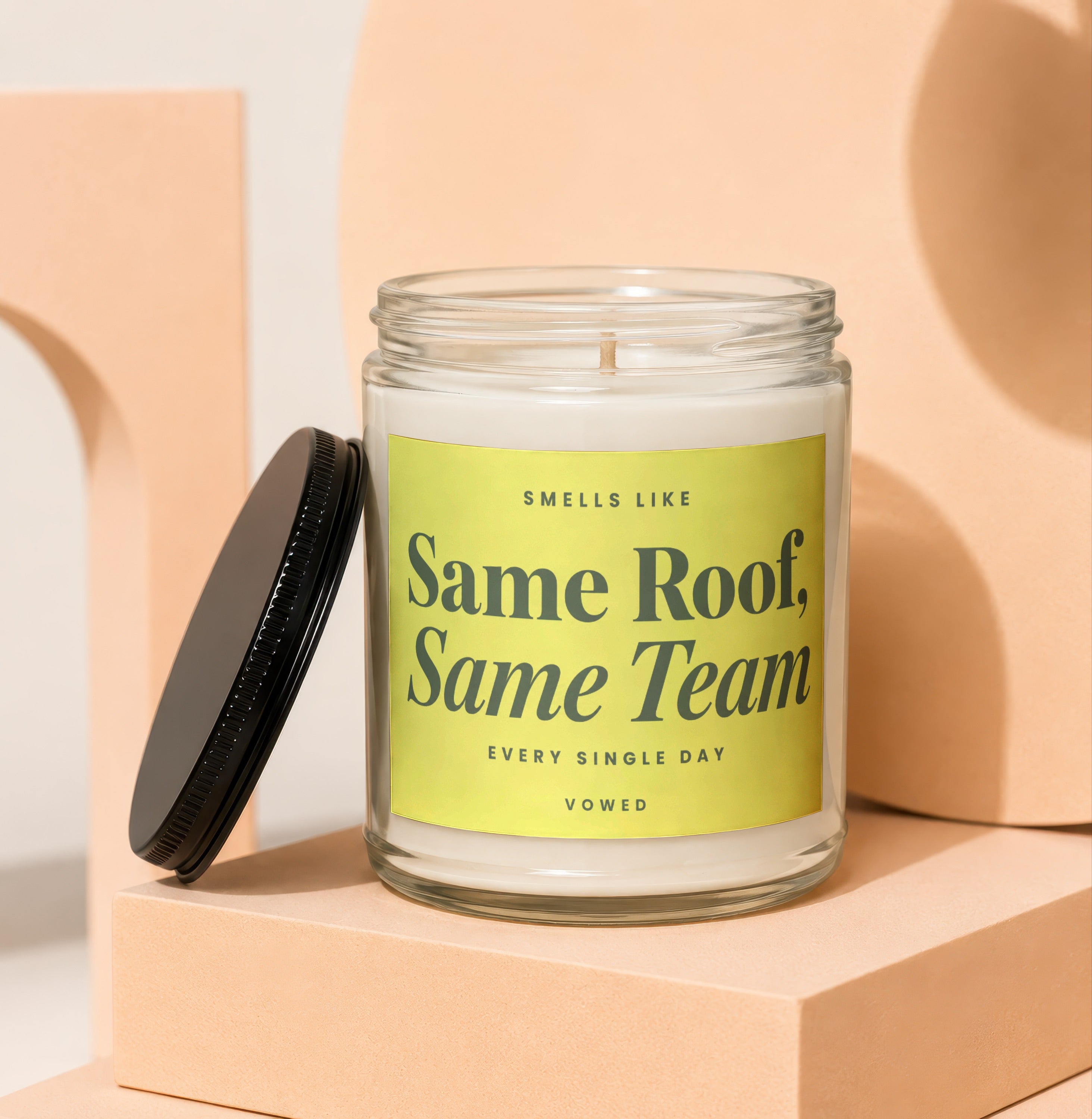 Glass jar candle with black lid, "Same Roof, Same Team" text on yellow label.