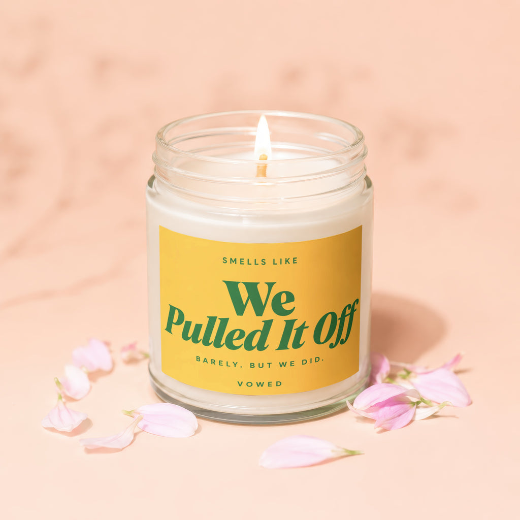 Glass candle with yellow label reading "Smells Like We Pulled It Off Barely, But We Did. Vowed."