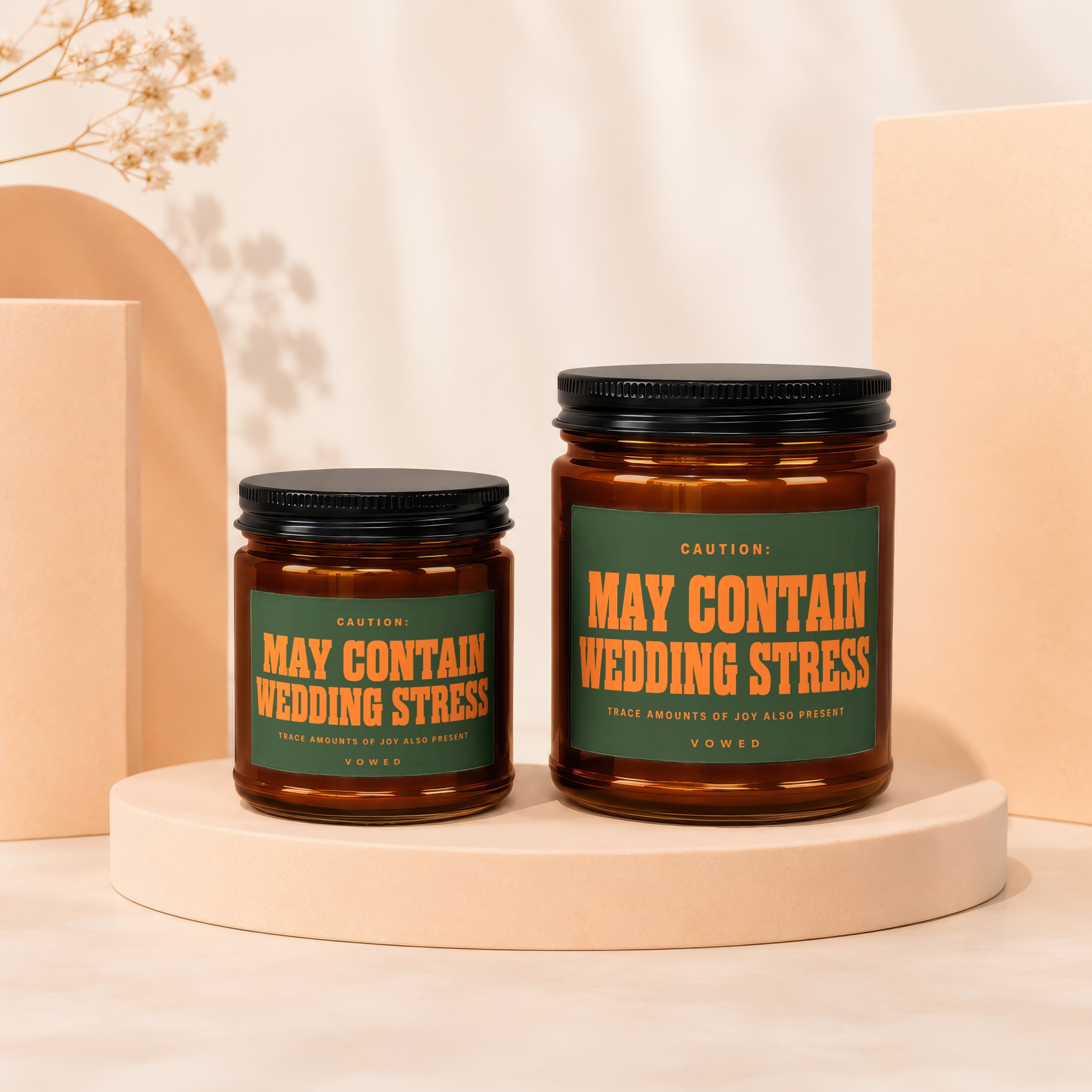 Two candles in amber jars with green labels reading "May Contain Wedding Stress".