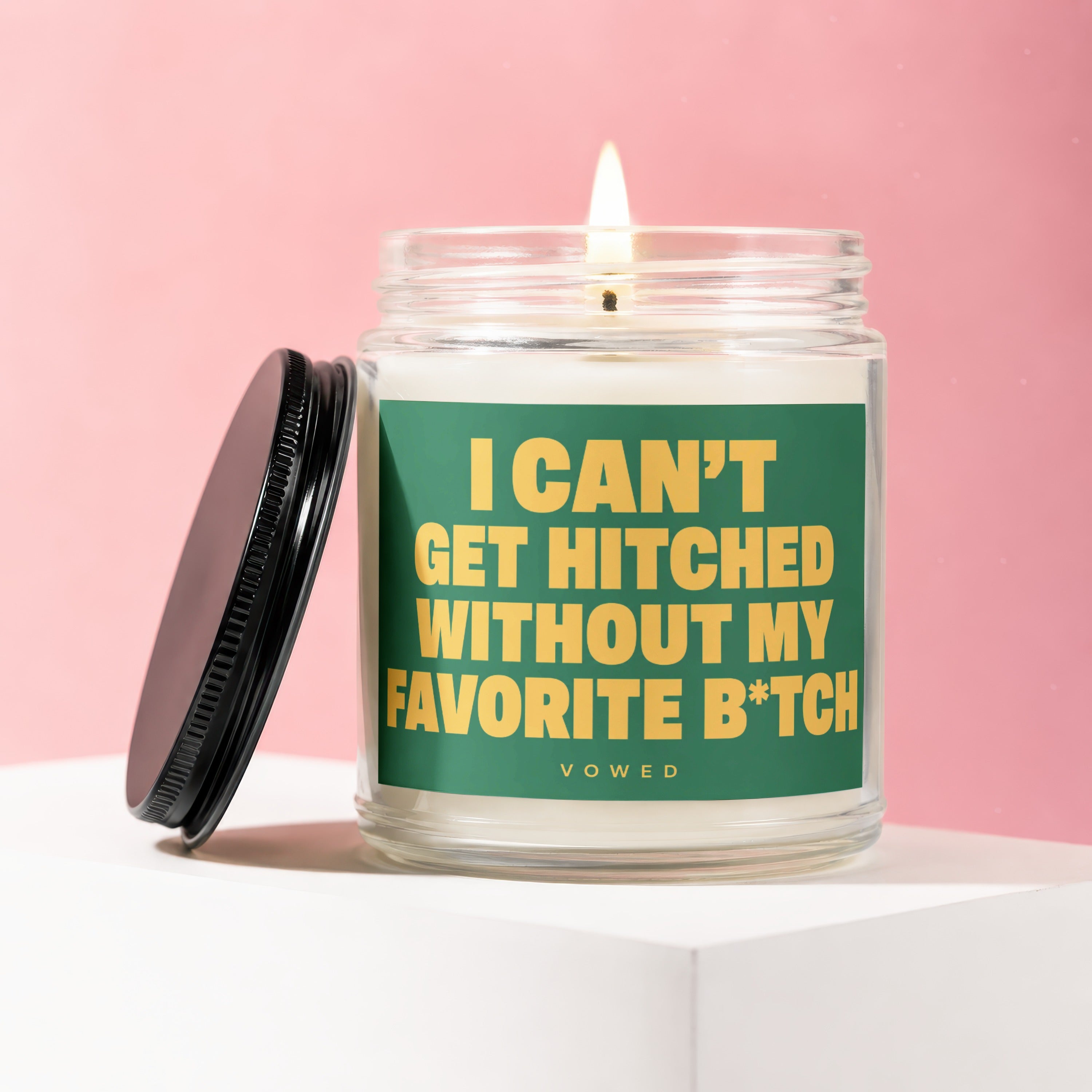 Glass candle with burning wick and black lid, featuring green label with yellow text.