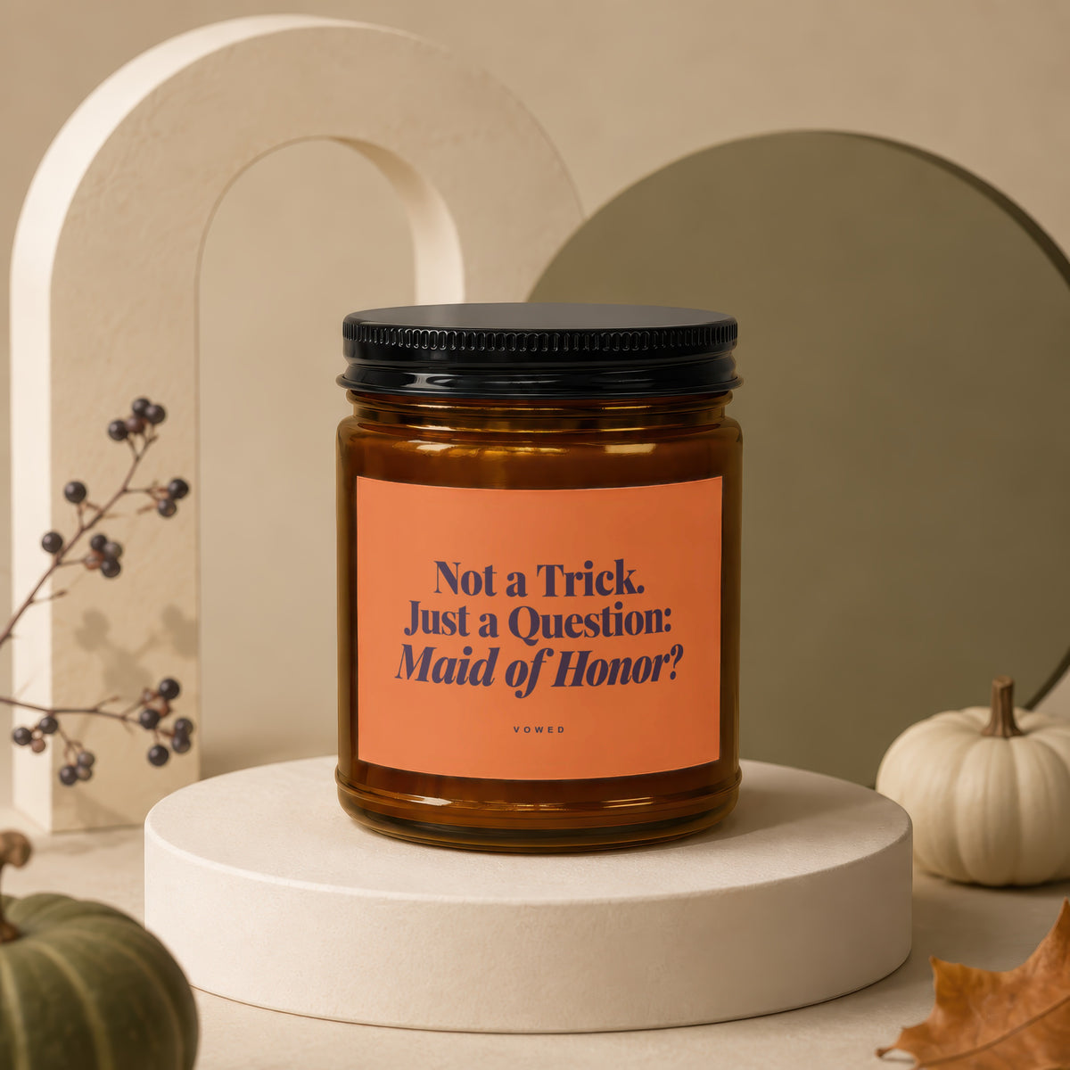 Amber candle with black lid and orange label that reads "Not a Trick. Just a Question: Maid of Honor?"