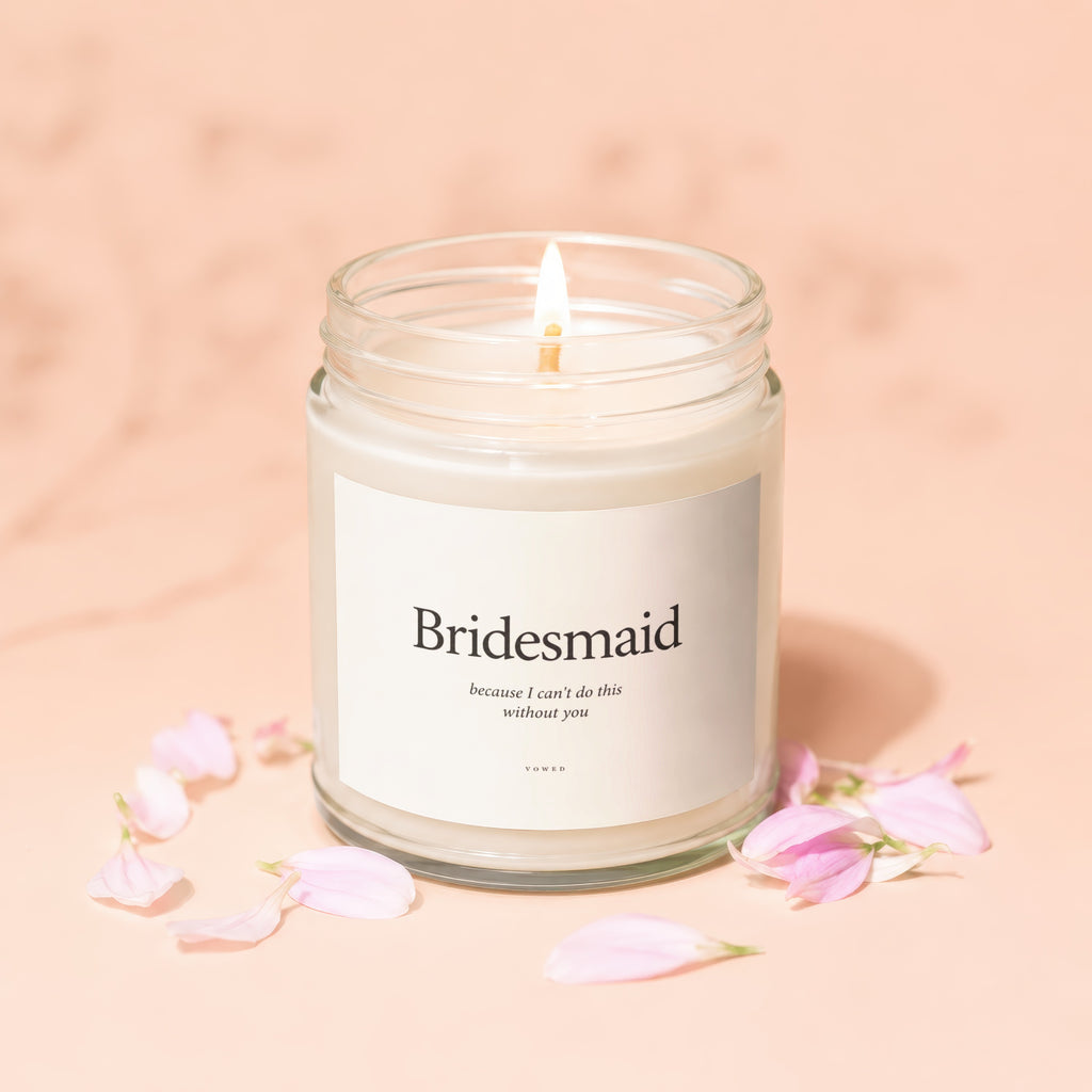 Bridesmaid candle with lit flame and pink petals, reads "because I can't do this without you."