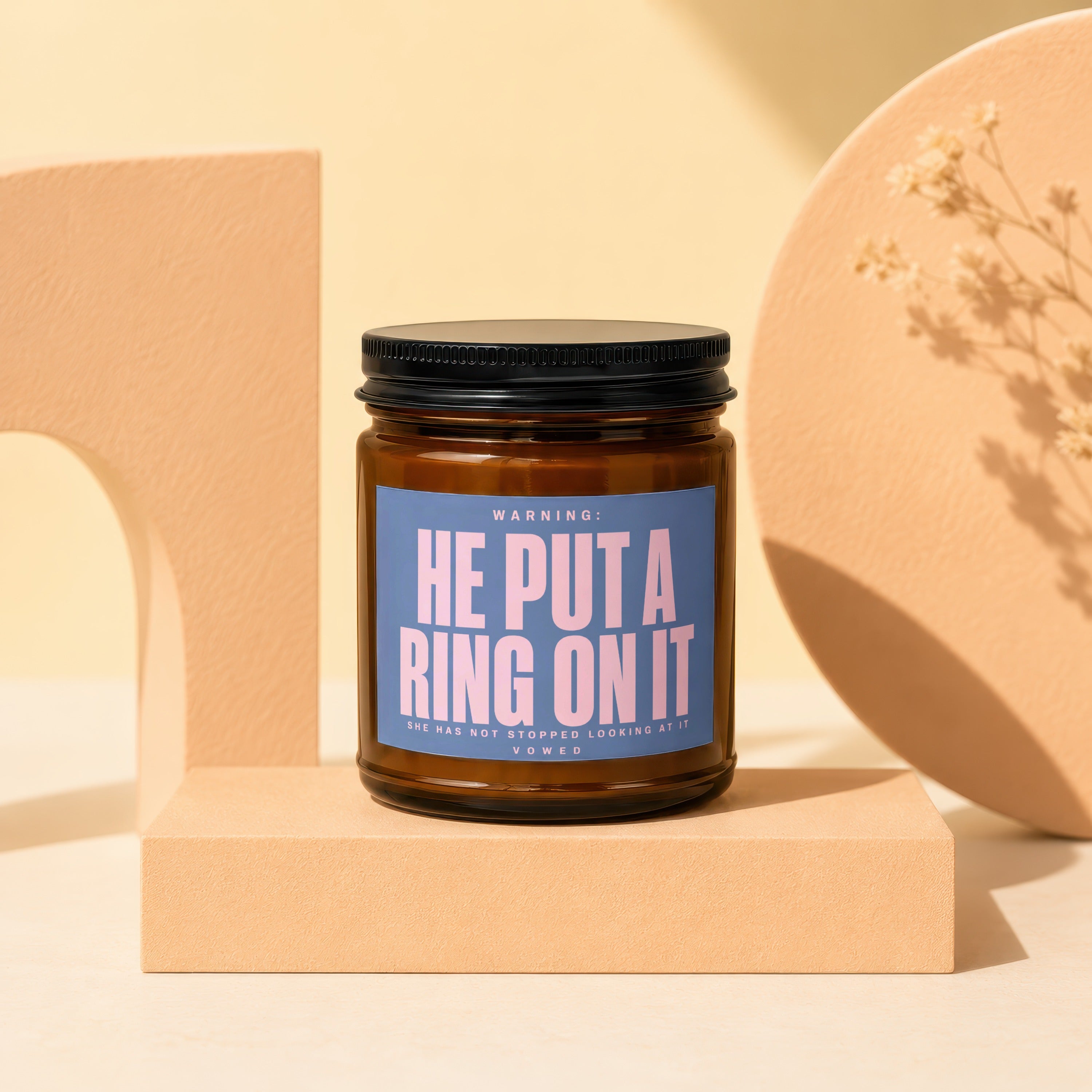 Brown glass candle with blue label text "HE PUT A RING ON IT".