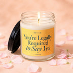 Glass candle with lit flame and yellow label reading "You're Legally Required to Say Yes".