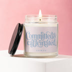 Candle with lit wick and "Committed & Caffeinated" text on label.