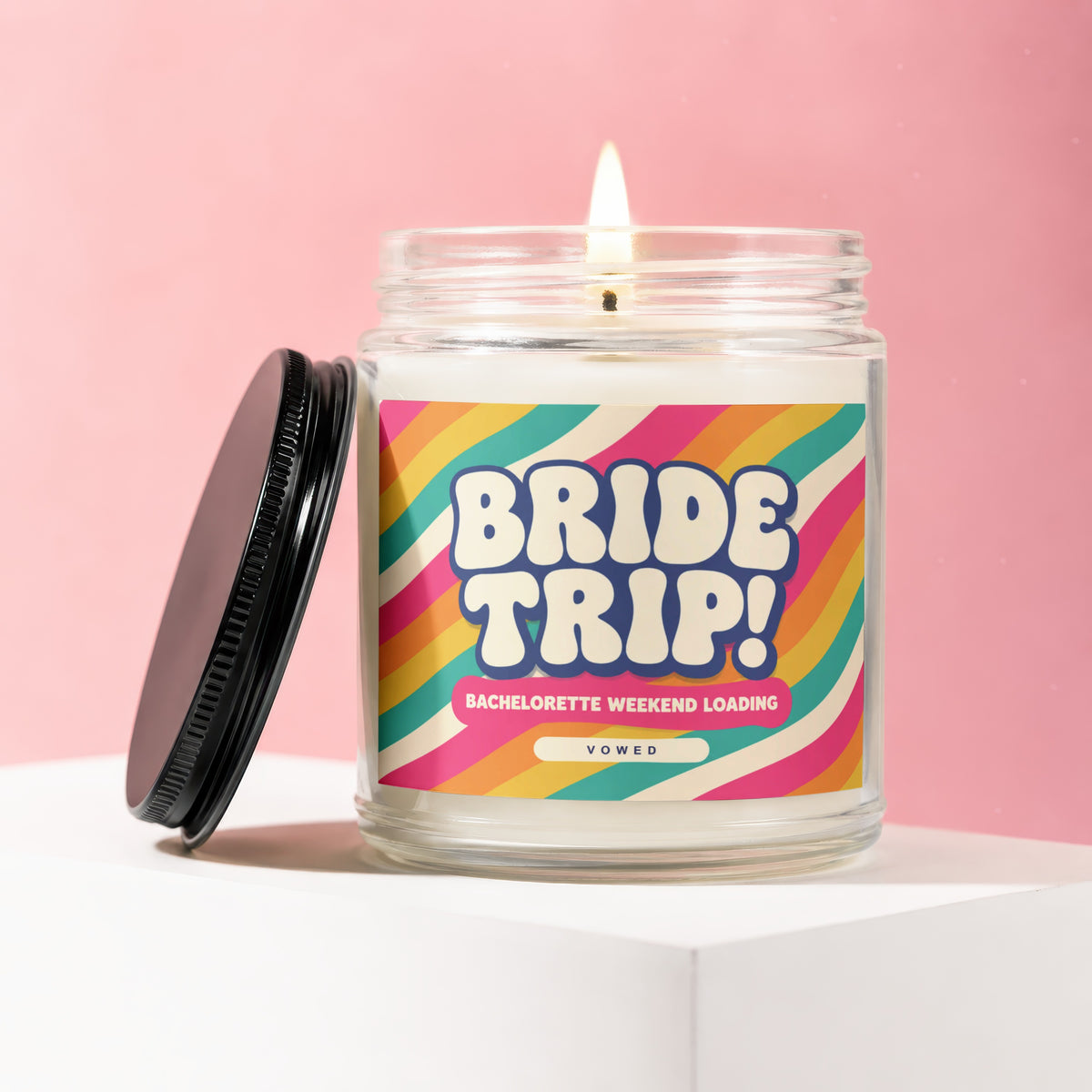 Glass candle with lit wick and "BRIDE TRIP!" text on rainbow label.