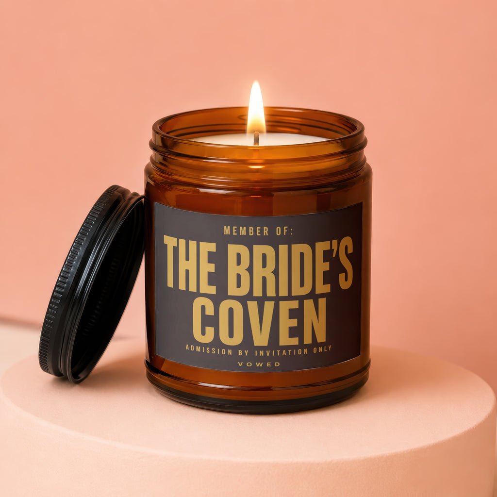 Amber jar candle with lit wick and black lid, reading "THE BRIDE'S COVEN".