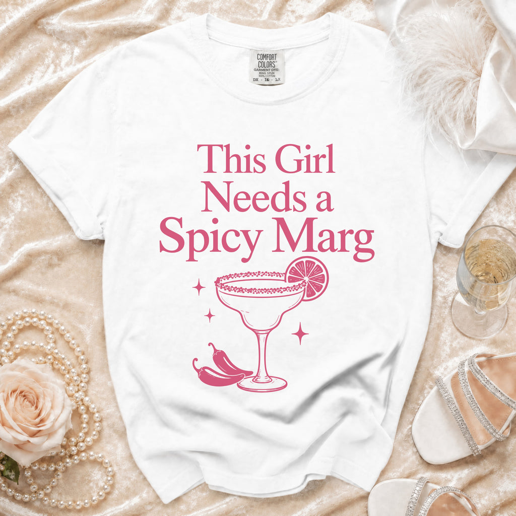 White t-shirt with pink text and graphic of "This Girl Needs a Spicy Marg" cocktail.